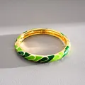 Close-up macro view of a gold-plated bangle with detailed green wave enamel finish - Gold-Green