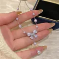 Macro detail of a sweet style necklace featuring a zircon bow pendant and pearls - Silver-Pink
