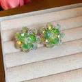 Macro view of flower stud earrings featuring iridescent and green faceted glass beads. - Green and White