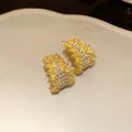 Macro view of gold C-shaped stud earrings with sparkling rhinestones and textured finish. - Gold