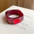Close-up detail of red marbled resin bangle with an oversized ruby-colored gemstone - Red