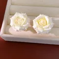 Close-up detail of elegant white rose stud earrings displayed on jewelry tray - White
