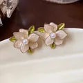 Close-up detail of French style floral stud earrings with pearl centers and enamel petals - White