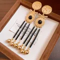 Detailed view of vintage gold-tone tassel earrings with cherub and Greek key patterns. - Portrait Relief Tassel Style / Silver Earring Post - Gold - Black