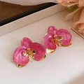 Primo piano di orecchini a perno a forma di orchidea rosa con accenti dorati e perno in acciaio. - Stud orecchini / Rosa