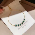 Detailed view of an elegant gold bracelet with green square zircons on a gift pouch - Style 16 Bracelet