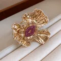 Detailed view of a gold-toned wrinkled flower cuff bracelet with sparkling pink rhinestones. - Gold