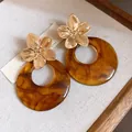 Detailed macro view of golden metal flower stud earrings with large amber resin circular pendants - Silver Earring Post - Coffee