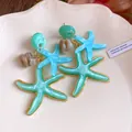Detailed view of teal resin starfish dangle earrings on a decorative plate. - Green
