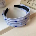 Dettaglio di un cerchietto in tessuto a righe blu e bianche con decorazioni pompon - Blu