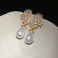 Primer plano de elegantes pendientes colgantes dorados con circonitas y perlas de lágrima - Dorado