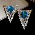 Macro detail of triangle stud earrings with vibrant blue gemstone and clear crystals - Blue