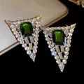 Close-up view of triangular earrings featuring a large emerald green center stone. - Green