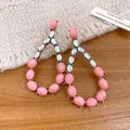 Primo piano di orecchini retrò con pietre rosa e cristalli iridescenti su legno. - Rosa