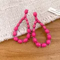 Dettaglio di orecchini a goccia rosa acceso con texture in pietra su fondo intrecciato. - Rosa Rosso