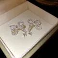 Dettaglio ravvicinato di eleganti orecchini a fiocco in argento con zirconi scintillanti e perni - Orecchini a Fiocco (HE33868) / Argento