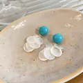 Nahaufnahme stilvoller Ohrringe mit blauen Harzperlen und schillernden weißen Muschelscheiben - Clip-Ohrringe / Blau-Weiß