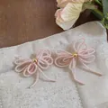 Gros plan de boucles d'oreilles nœuds en perles de verre roses sur support en tissu - Boucles d'Oreilles Clous Nœud Perles / Rose