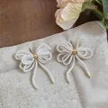 Gros plan d'élégantes boucles d'oreilles nœud en perles de verre blanches fait main. - Boucles d'Oreilles Clous Nœud Perles / Blanc