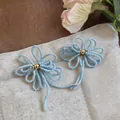 Gros plan de boucles d'oreilles fleurs en perles bleu clair avec centre doré sur tissu - Boucles d'Oreilles Clous Nœud Perles / Bleu