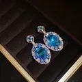 Vista dettagliata di orecchini di lusso con zirconi blu e alone scintillante in box - Orecchini (Perno in argento) / Argento-Blu