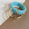 Close-up view of a light blue resin bangle set with gold starfish and pearl details for beach style - Gold, Blue