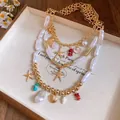 Detailed view of a gold layered necklace with baroque pearls, starfish, and shell charms. - Gold-White