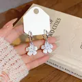 Macro view of exquisite white zircon flower hoop earrings held against a vintage book. - Flower Style (HE32902) / Silver
