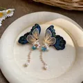 Detailed close-up of embroidered butterfly earrings with pearl tassels and gold accents. - Blue