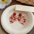 Close-up of colorful resin leaf earrings with red studs on a textured plate - Leaf Style (HE32524) / Red