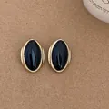 Macro view of vintage gold-framed black oval stud earrings on textured background - Oval Stud Earrings - Silver Earring Post / Black