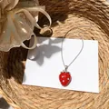 Close-up of a red resin strawberry necklace with sparkling rhinestone studs in natural light. - Red