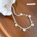 Macro view of dainty white resin flower beads and green leaf charms on a beaded necklace - White-Yellow