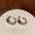 Detailed macro view of elegant silver C-shaped hoop earrings with red heart zircons - Heart C-Shaped / Silver/Pink