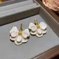 Macro view of elegant white enamel flower stud earrings with detailed golden edges. - White