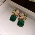 Detail shot of diamond-encrusted panda earrings with green square gemstone pendants - Green
