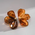 Macro view of oversized amber marbled resin flower stud earrings with golden stamen details. - Brown