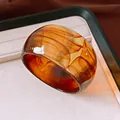 Close-up of a wide acrylic resin bangle with amber marbled texture on a display tray - Brown