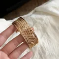 Detailed close-up of an intricate gold mesh metal cuff bracelet with woven texture. - Woven Mesh Style / Gold