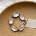 Close-up of a gold-toned bracelet featuring five faceted oval stones and a toggle clasp. - Five Stone Mother-of-Pearl Texture Style / Gold-White