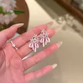 Nahaufnahme von rosa Emaille-Schleifen- und Zirkon-Blumenohrringen in der Hand. - Schleife Ohrstecker (HE31014) / Rosa