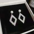 Macro shot of elegant geometric rhombus earrings featuring pavé crystals and white pearls - Rhombus Pearl Style / Silver
