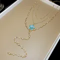 Close-up of a layered gold necklace with pearls and a blue floral pendant detail - Layered Style / Gold Blue