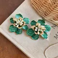 Detail view of green enamel flower earrings with golden accents on a vintage background - Green