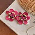 Detailed macro view of enamel flower stud earrings with intricate golden edges and stamens. - Rose Red / Gold