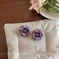 Dettaglio ravvicinato di orecchini a rosa 3D viola su un morbido cuscino color crema - Lavanda