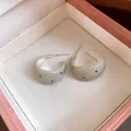 Detailed view of cream enamel C-shaped earrings with blue polka dots in a pink jewelry box - Gray