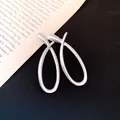 Detailed close-up view of polished silver hollow cross earrings on a vintage book background - Silver