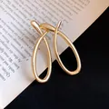 Macro detail of minimalist golden twisted hollow drop earrings on a book background - Gold