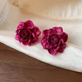 Detailed macro view of elegant magenta resin rose stud earrings on luxurious silk fabric - Silver Earring Post Style / Rose Red